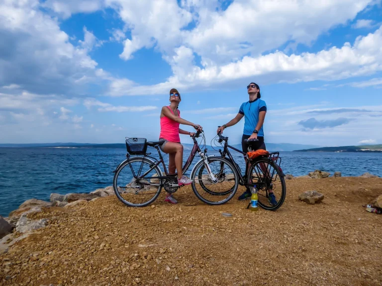 A couple in sporty outfits, standing on their bikes and checking the weather. Behind them there is Mediterranean Sea. Thick clouds above them. Active holidays. Beautiful coastal line of Croatia