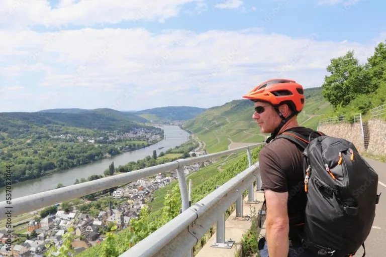 Man with bright orange bike helmet looking out over a panoramic view of the Moselle river